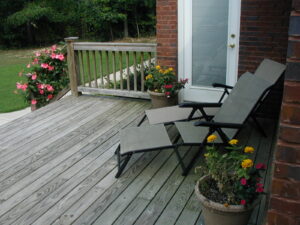 A deck with two lawn chairs and flowers.