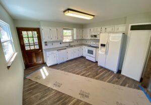 A kitchen with white cabinets and wood floors.