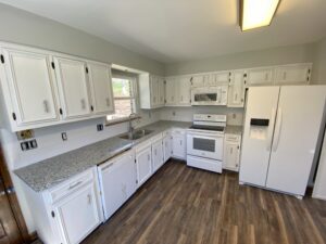 A kitchen with white cabinets and wood floors.