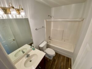 A bathroom with white walls and wooden floors.