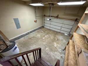 A garage with the floor in disrepair and stairs leading to it.