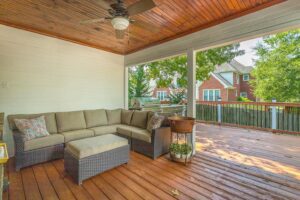 A patio with a couch and ottoman on the back porch.