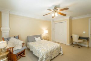 A bedroom with a bed, chair and ceiling fan.