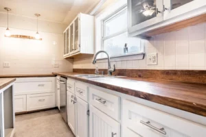 A kitchen with white cabinets and wood countertops.