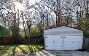 A white garage with two doors in the middle of a yard.