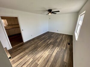 Empty room with hardwood floors and a fan.