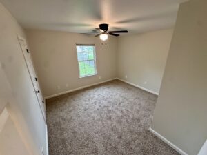 Empty carpeted room with ceiling fan and window.