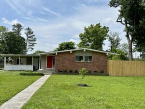 Brick ranch house with red door and fenced yard.