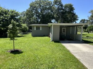 Grey house with a green lawn and trees.