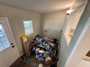 Cluttered room with paint supplies and ladders.