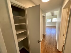 Open white closet in hallway with hardwood floor.