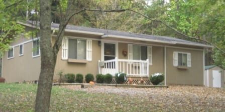 Beige ranch house with porch and wooded yard