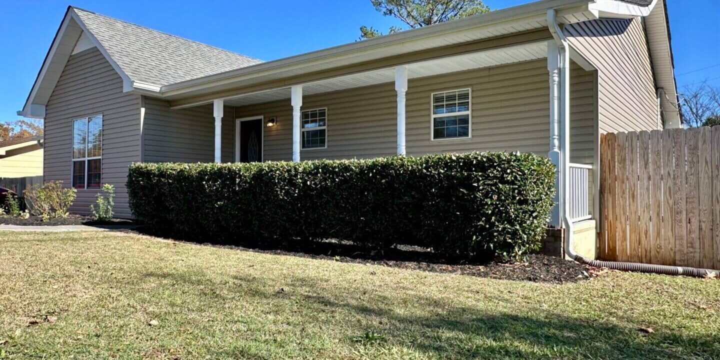 Suburban house with beige siding and neatly trimmed hedge.