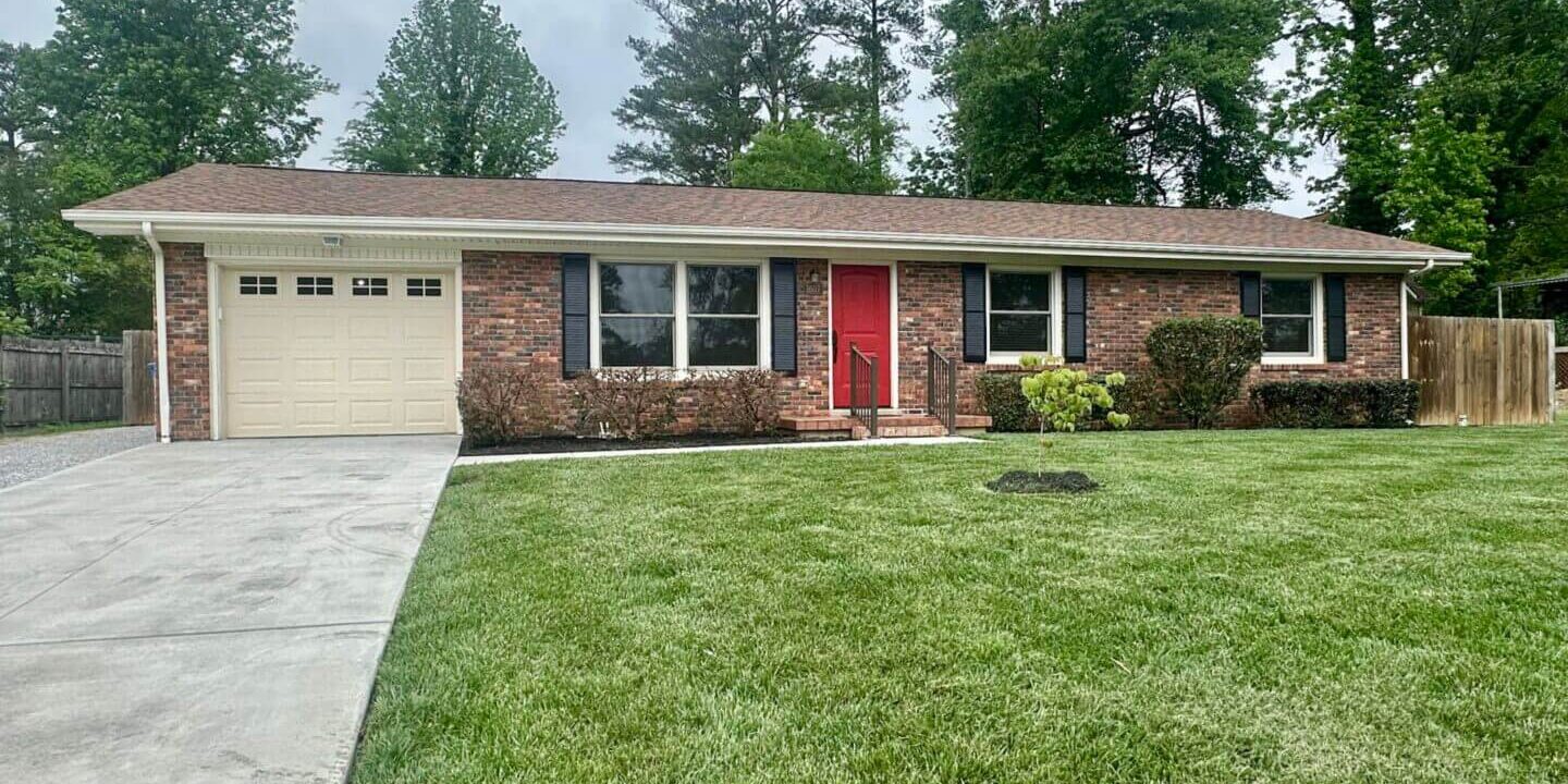Single-story brick house with a red front door and a well-maintained lawn.