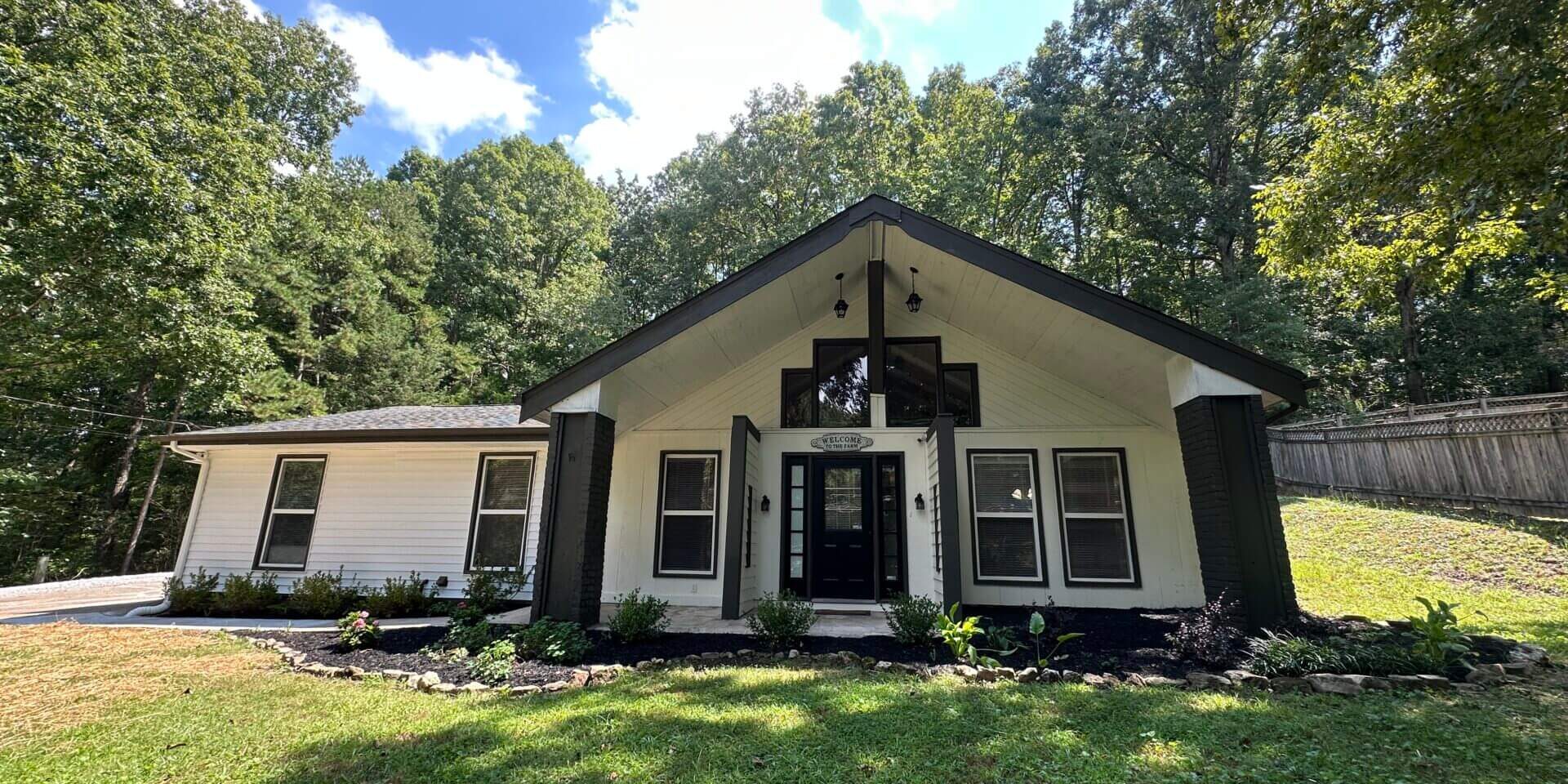Cozy single-story white house with black shutters surrounded by trees.