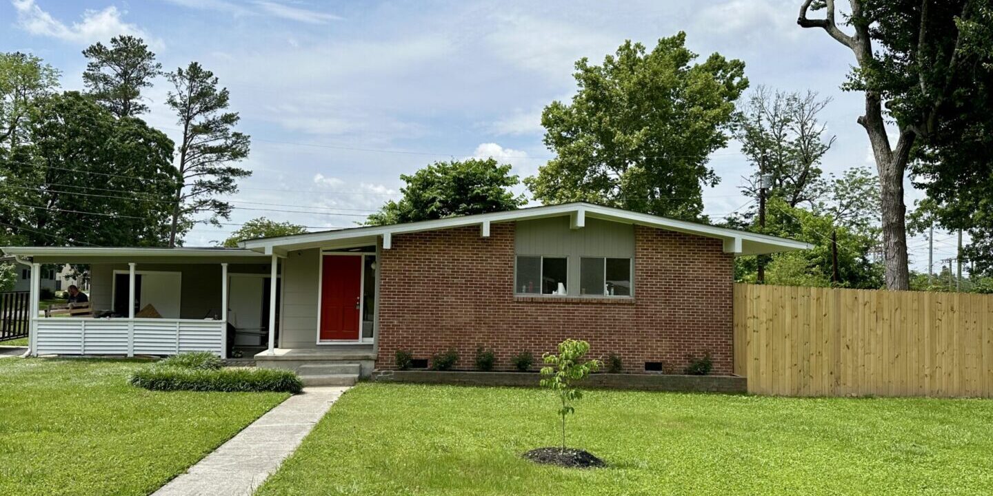Brick ranch house with red door and fenced yard.
